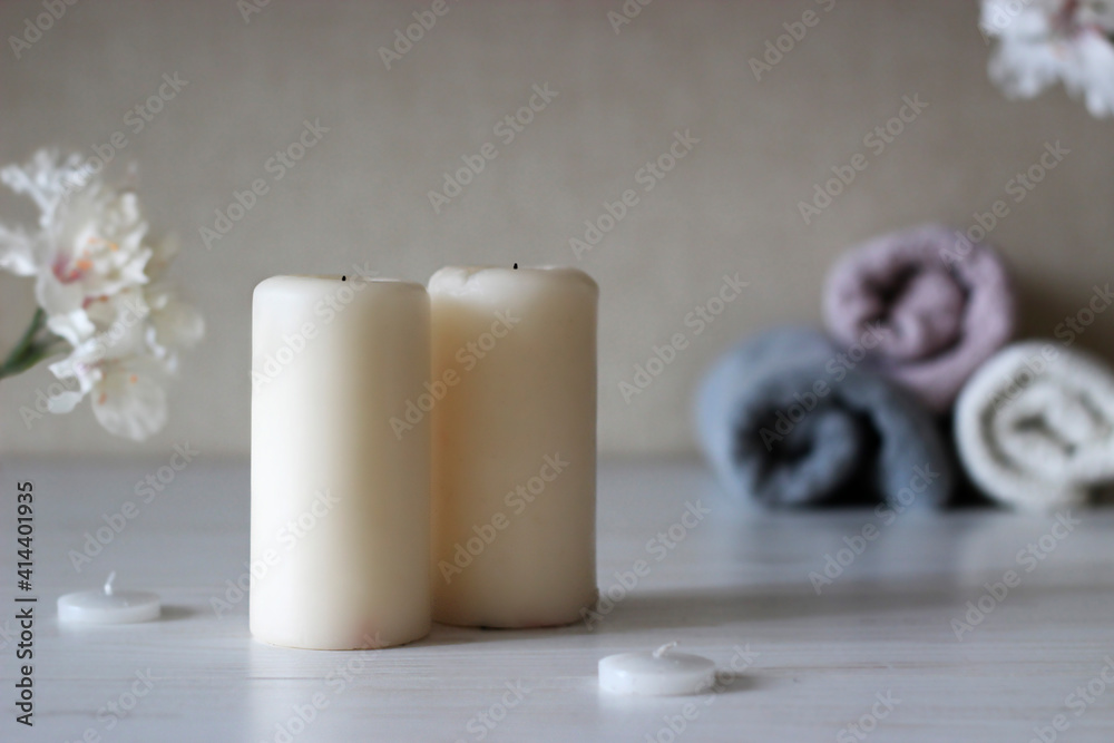 two large candles and 2 small candles stand against a background of folded towels on a brown background