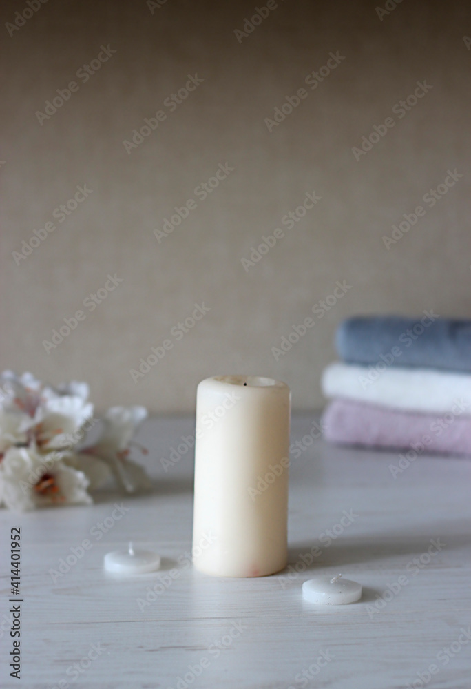 a light candle stands on the table against the background of rolled towels and flowers