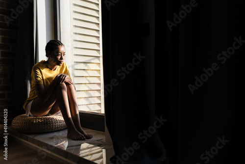 Attractive young african woman sitting on a windowsill