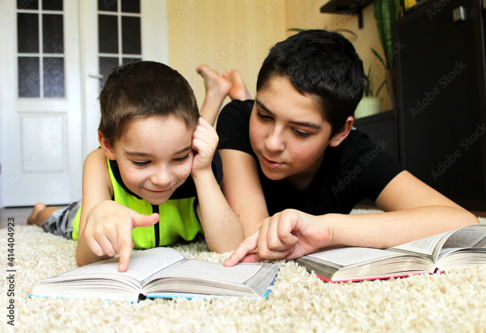 Children read books together. The older brother helps the younger one with his homework. Children read books together. The older brother helps the younger one with his homework.