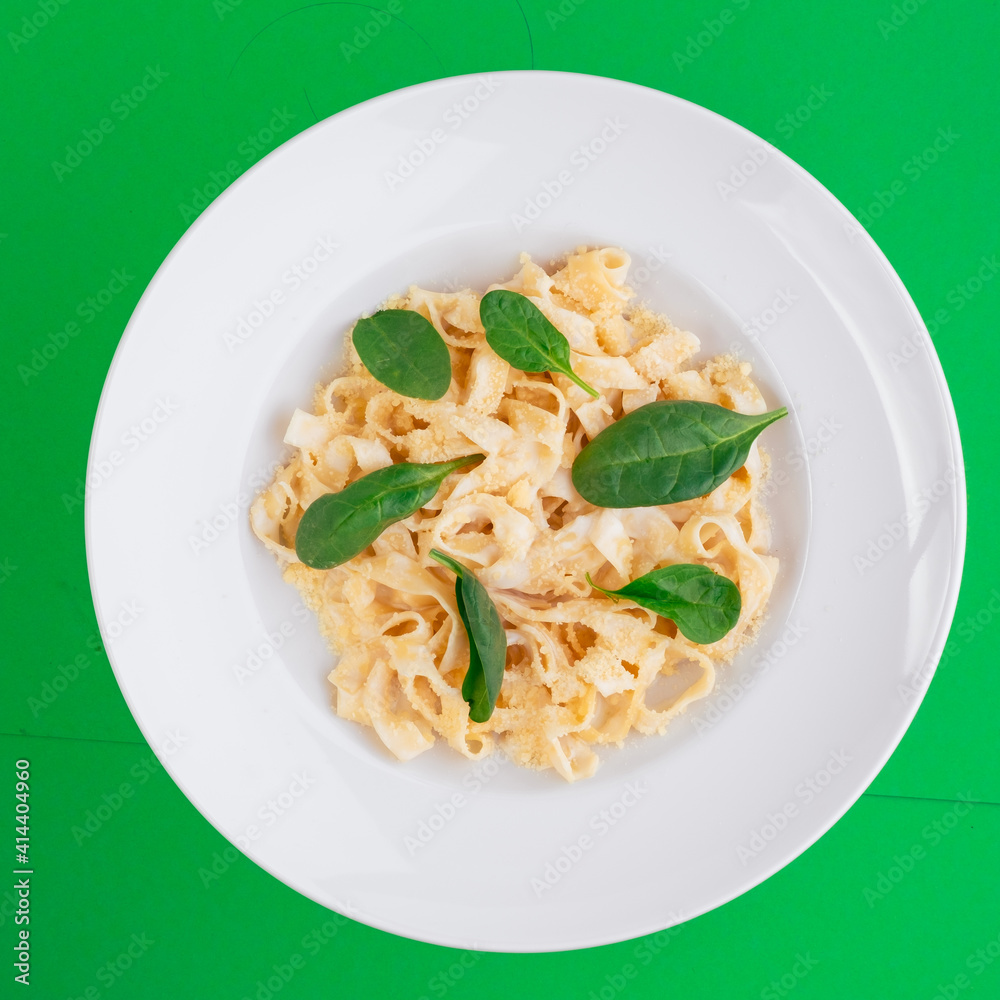 Tagliatelle pasta with cheese in a white plate on green background. Top view. Close up. Photo for clipping, for the menu