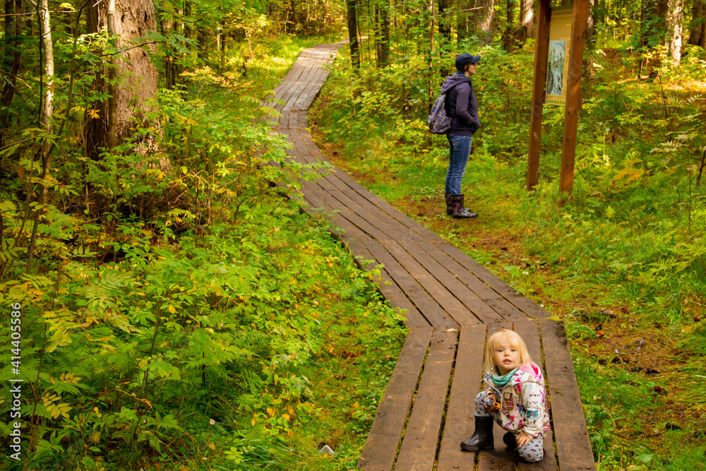 Mother and daughter are traveling. Mother and daughter are walking along the path of the nature reserve in the forest. Mother and daughter are traveling. Mother and daughter are walking along the path of the nature reserve in the forest.