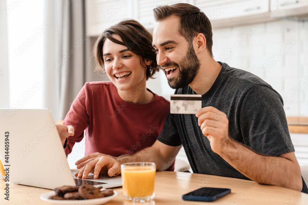 Happy young couple using laptop and credit card while sitting at home Happy young couple using laptop and credit card while sitting at home