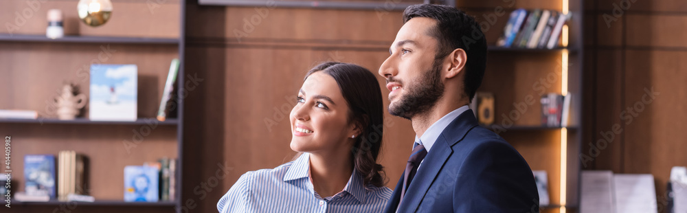 happy multicultural business partners smiling while looking away in restaurant, banner happy multicultural business partners smiling while looking away in restaurant, banner