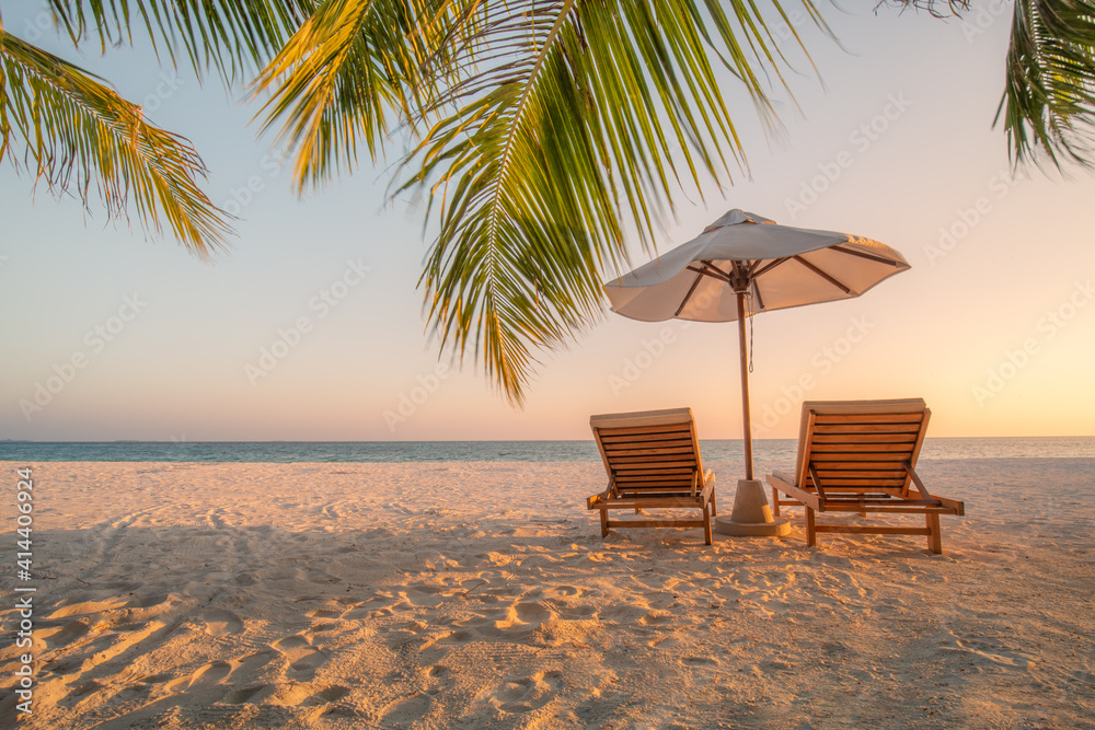 Obraz premium Beautiful tropical sunset scenery, two sun beds, loungers, umbrella under palm tree. White sand, sea view with horizon, colorful twilight sky, calmness and relaxation. Inspirational beach resort hotel