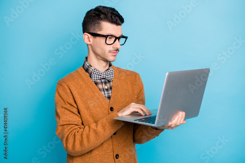 Photo of serious focused young handsome man write hold laptop wear bow tie isolated on blue color background