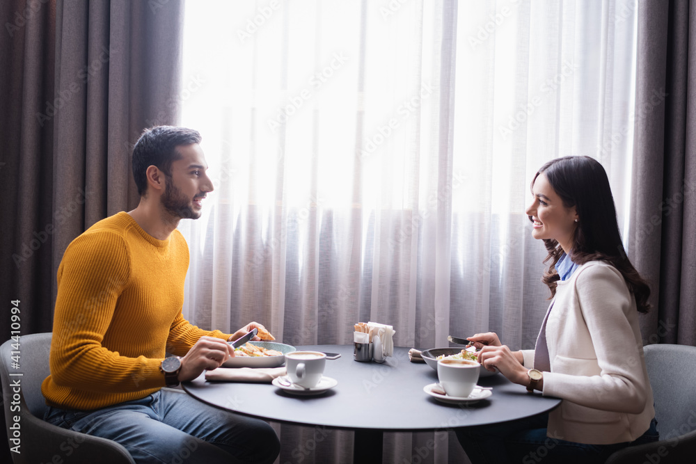 Cheerful interracial couple looking at each other while dinning in restaurant Cheerful interracial couple looking at each other while dinning in restaurant