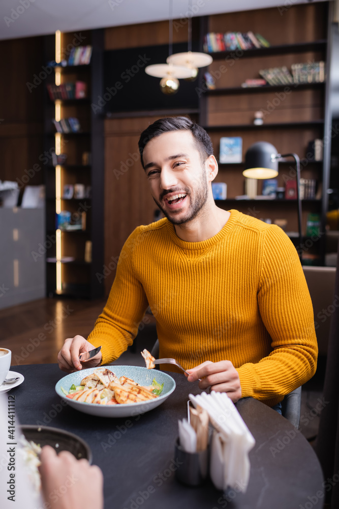 Cheerful arabian man dinning with girlfriend on blurred foreground in modern restaurant
