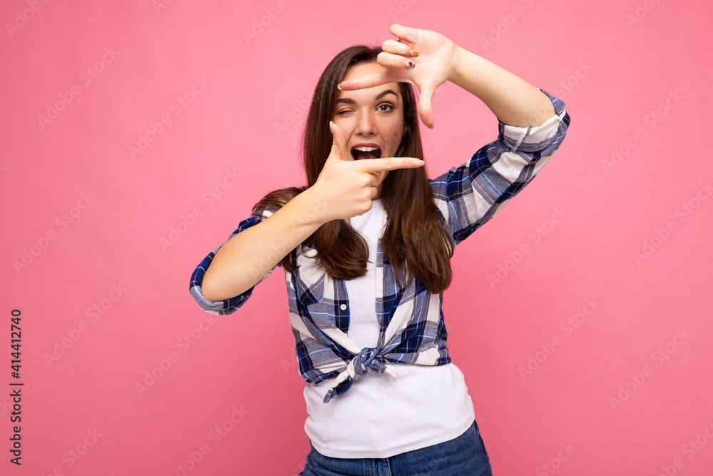 Young positive delightful pretty brunette woman with sincere emotions wearing hipster check shirt making frame with hands, taking picture with imaginary camera and standing isolated on pink background Young positive delightful pretty brunette woman with sincere emotions wearing hipster check shirt making frame with hands, taking picture with imaginary camera and standing isolated on pink background