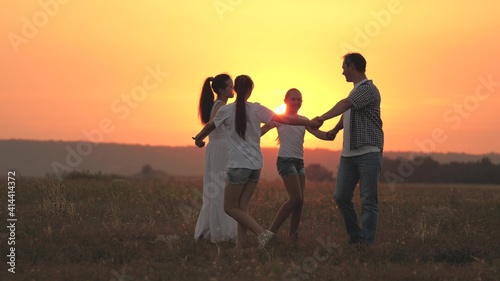 A happy family, a young mother, dad and daughters play and dance together in the sun, have fun in field. Children with parents play in park on grass at sunset. Happy family childhood and health