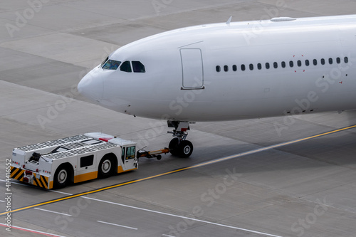 The apron transporter tows a modern narrow-body white passenger aircraft across the airfield of an international airport. © fifg