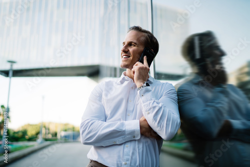 Smiling man speaking on cellphone near glass wall