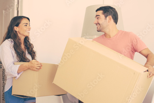 Happy young couple moving into new apartment, carrying carton boxes, looking around and smiling. Real estate or property buying concept © Mangostar