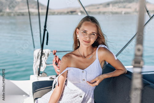 Portrait of a young and beautiful girl with fairy hair, sitting and posing on her white yacht on a clear sunny day against the backdrop of the water. Casual concept