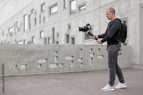 filmmaking, hobby and creativity concept - full length portrait of professional videographer shooting video using modern dslr camera on 3-axis gimbal over concrete building photo