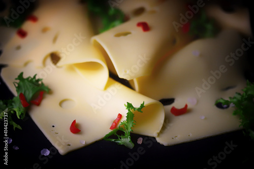 Slices of cheese with spices on a black background.