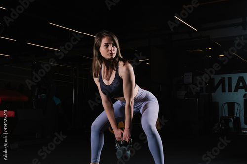 Young woman with athletic body poses sexy with kettlebell. Young woman looks beautiful in the gym.