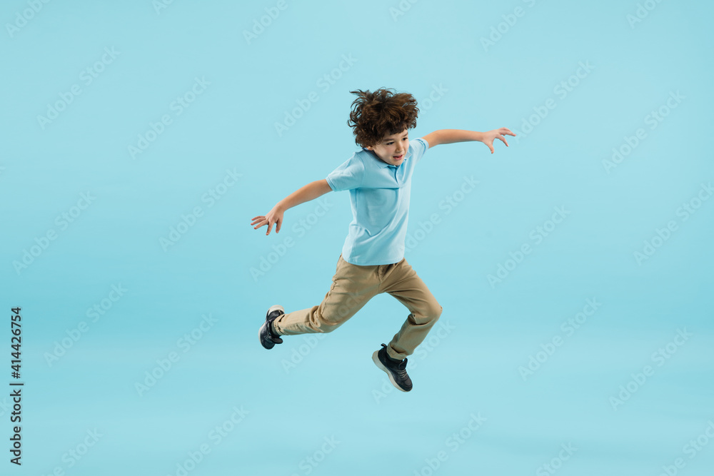 Flying, jumping high. Childhood and dream about big and famous future. Pretty little boy isolated on blue studio background. Dreams, imagination, education, facial expression, emotions concept. Flying, jumping high. Childhood and dream about big and famous future. Pretty little boy isolated on blue studio background. Dreams, imagination, education, facial expression, emotions concept.