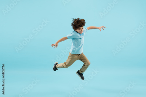 Flying, jumping high. Childhood and dream about big and famous future. Pretty little boy isolated on blue studio background. Dreams, imagination, education, facial expression, emotions concept.