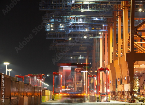 Cranes in the container harbour port during logistic loading process at night time with artificial lights during work