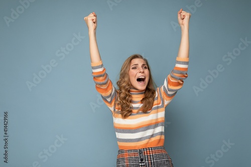 Photo portrait of young pretty beautiful happy positive funny joyful blonde woman with sincere emotions wearing striped pullover isolated on blue background with empty space and celebrating winning
