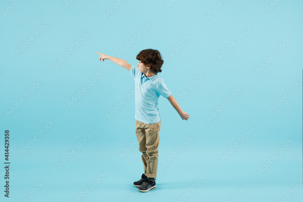 Pointing out, showing. Childhood and dream about big and famous future. Pretty little boy isolated on blue studio background. Dreams, imagination, education, facial expression, emotions concept. Pointing out, showing. Childhood and dream about big and famous future. Pretty little boy isolated on blue studio background. Dreams, imagination, education, facial expression, emotions concept.