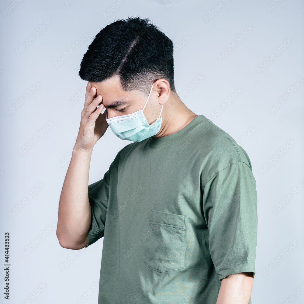 Stressful COVID-19 Coronavirus portrait handsome young asian .man wearing green shirt and mask protection from covid 19 isolated on gray background in studio. Asian man people. COVID-19 concept.