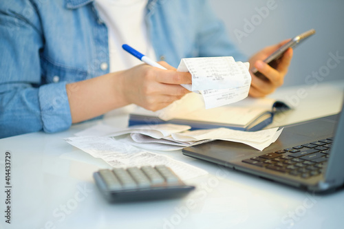 woman using a pen writing on bank account book while holding the bills to calculate in living room at home. Expenses, account, taxes, home budget concept photo
