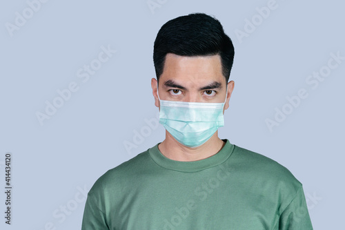 Stressful COVID-19 Coronavirus portrait handsome young asian .man wearing green shirt and mask protection from covid 19 isolated on gray background in studio. Asian man people. COVID-19 concept.