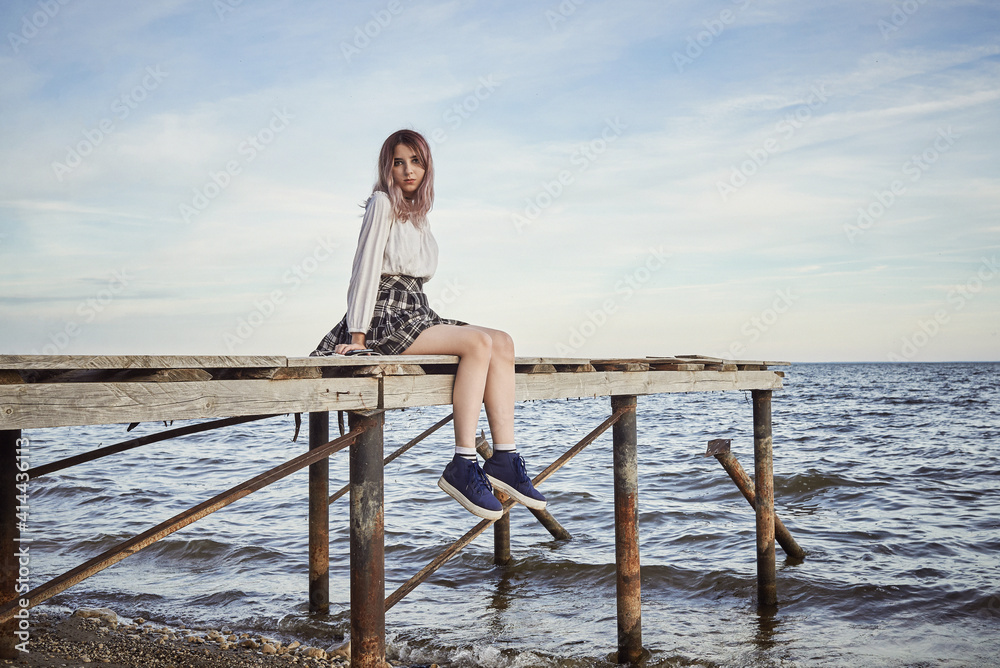 a sad young beautiful girl sits on the catwalk against the sea. summer landscape