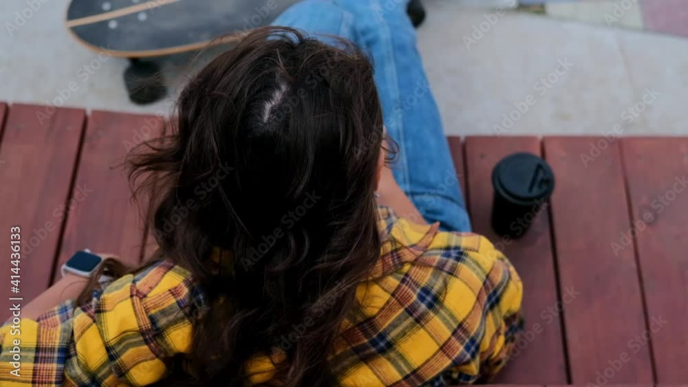 An active young woman, freelancer, works in the park on a laptop, planning to ride her skateboard home afterwards. People miss the freedom to move around the street after quarantine.