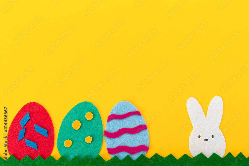 Easter holiday. Cut out of felt applications of eggs and a rabbit on the grass. Yellow background. Flat lay. Copy space