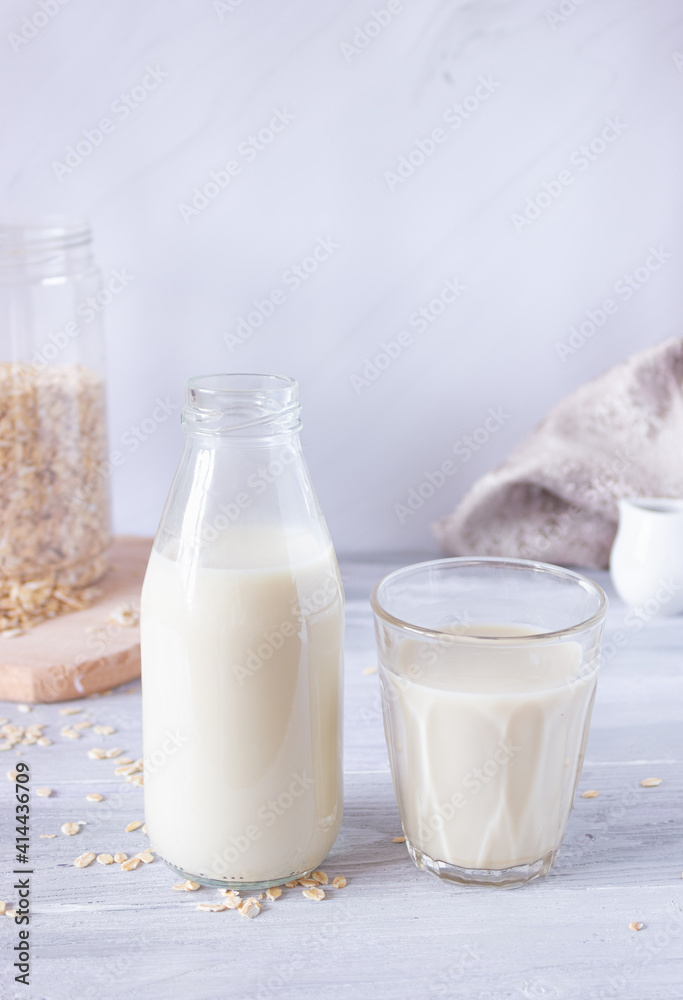 Vegetable oat milk in a glass bottle and in a glass cup on a light background. Healthy drinks, vegetarianism. Side view. Vertical photo Vegetable oat milk in a glass bottle and in a glass cup on a light background. Healthy drinks, vegetarianism. Side view. Vertical photo