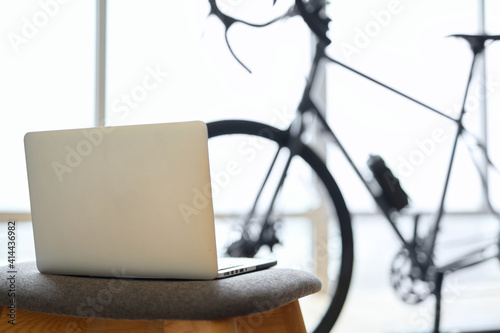Modern laptop with bicycle trainer on blurred background