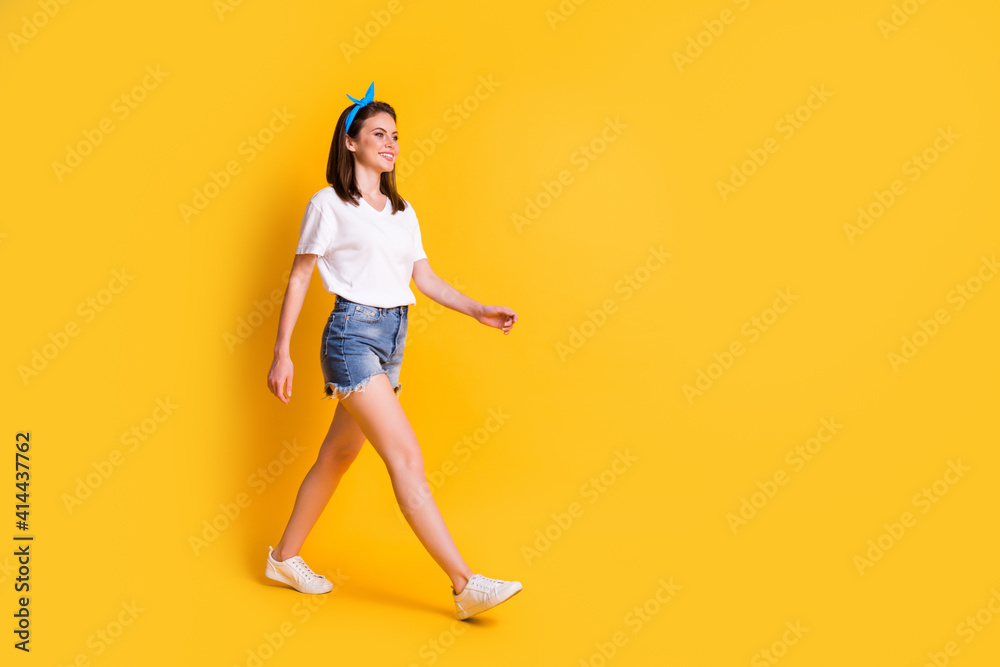 Full body profile side photo of beautiful brown haired girl wear blue pin up white t-shirt good mod walk isolated on yellow background