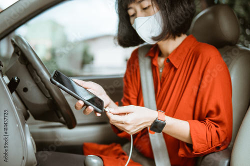 asian Woman in protective mask driving a car on road. charge her phone