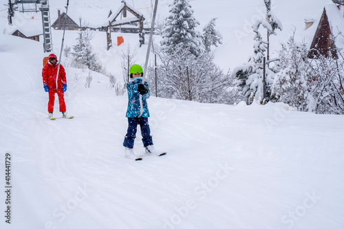 AURON, FRANCE-01.01.2021: Professional ski instructor and child lifting on the ski drag lift rope to the mountain during snowfall. Family and children active vacation concept. Blurred focus background