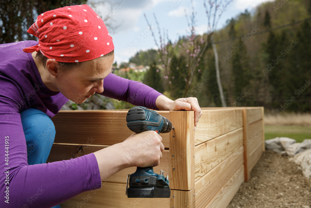 Woman screwing wooden frame for a raised garden bed.