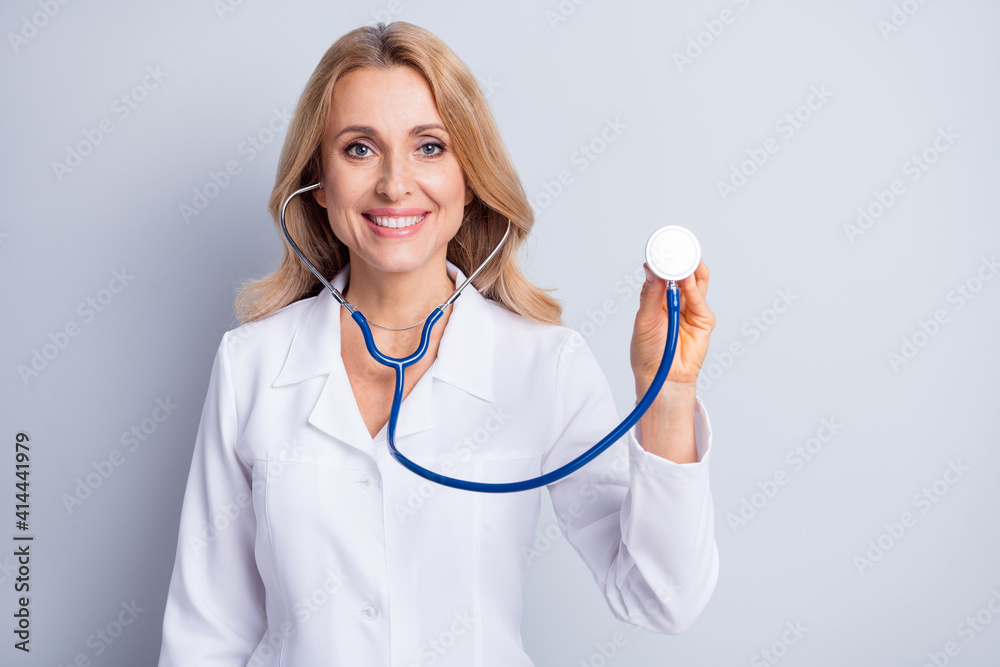Photo of mature positive smiling cheerful doctor woman hold stethoscope listen breathing isolated on grey color background Photo of mature positive smiling cheerful doctor woman hold stethoscope listen breathing isolated on grey color background