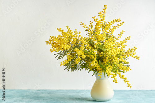 Vase with mimosa flowers on white background photo