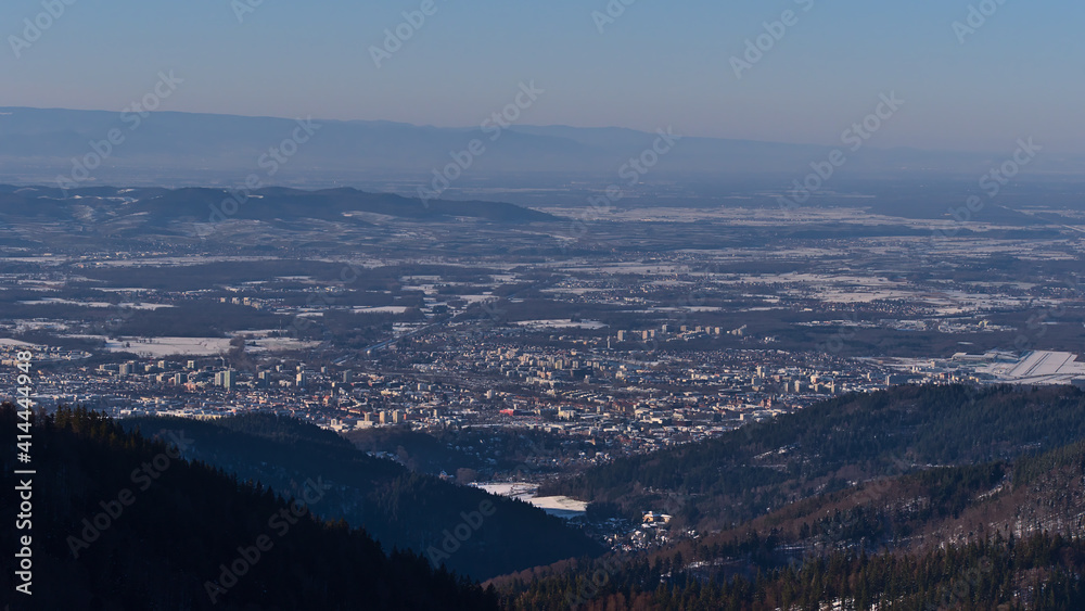 Beautiful aerial view of city Freiburg im Breisgau, Kaiserstuhl hills and Vosges mountain range on horizon in winter with snow-covered landscape viewed from Schauinsland peak, Black Forest, Germany.