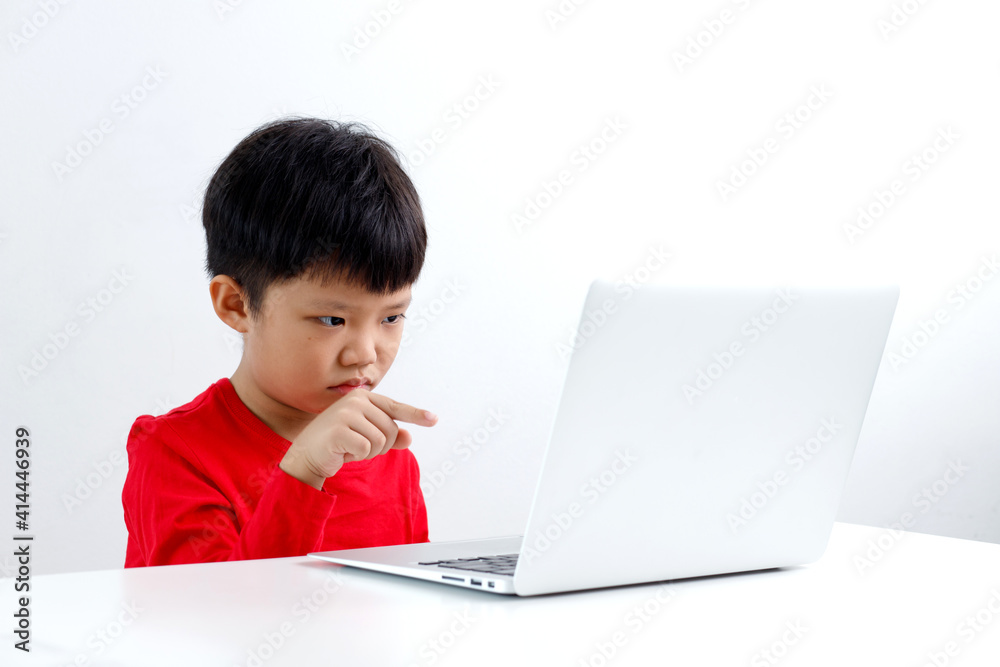 Portrait of frustrated little Asian boy pointing at the computer screen, sitting at a desk and doing homework. E-learning and education concept. Portrait of frustrated little Asian boy pointing at the computer screen, sitting at a desk and doing homework. E-learning and education concept.