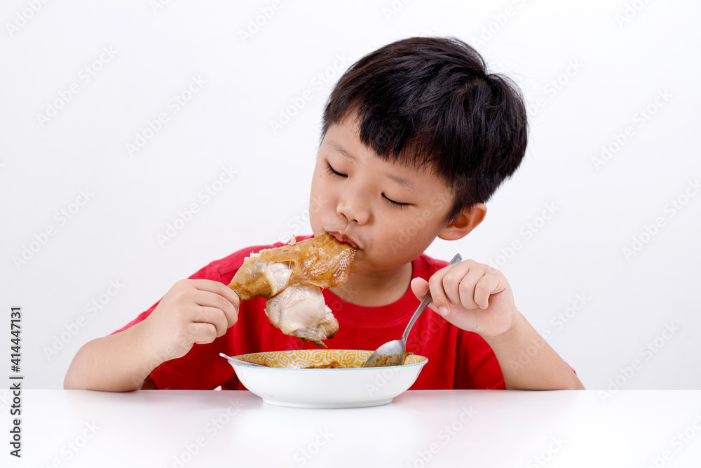 Portrait of cute little Asian boy enjoying eating chicken drumstick with noodles at home, isolated on white background. Portrait of cute little Asian boy enjoying eating chicken drumstick with noodles at home, isolated on white background.