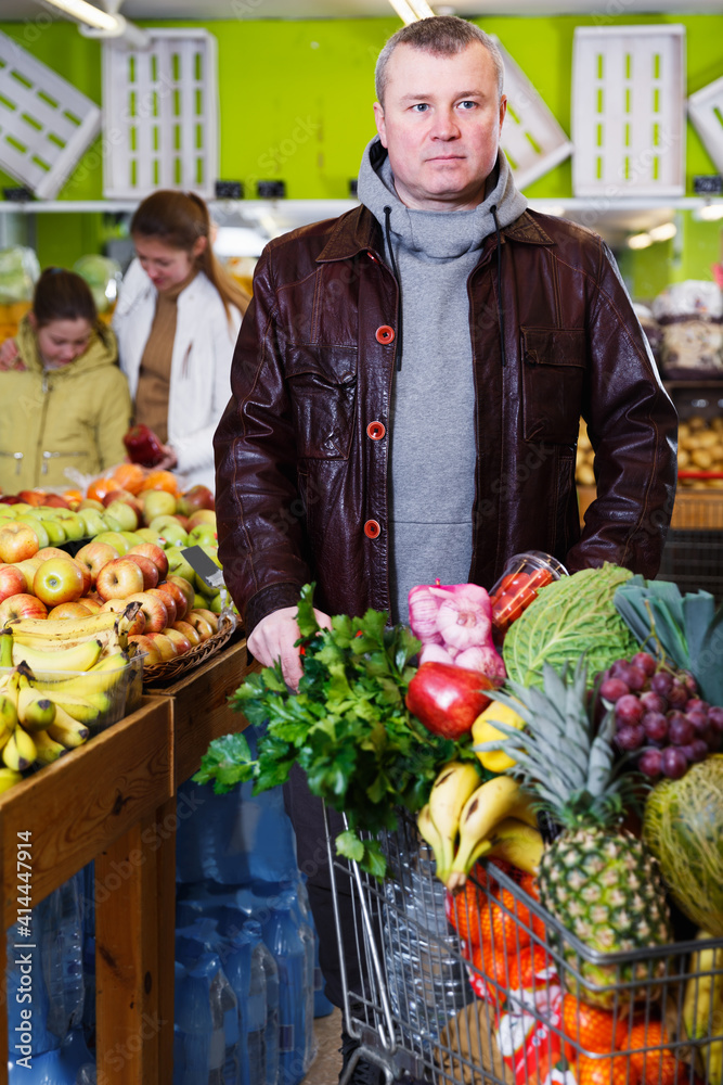 Serious concentrated man standing in fruit market with shopping cart