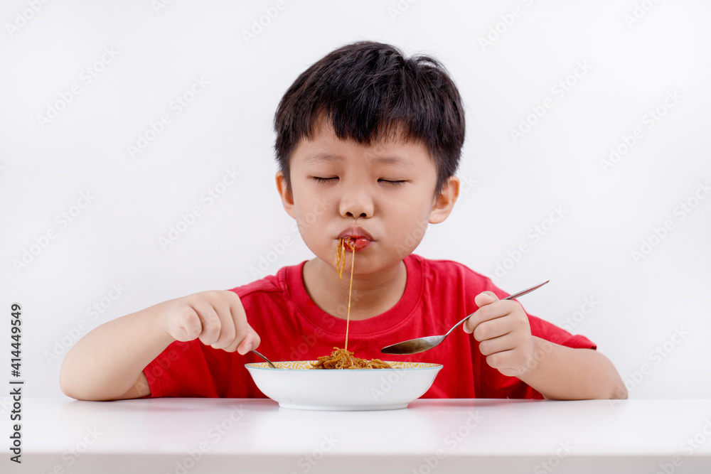 Cute little Asian boy enjoying eating noodles at home, isolated on white background Cute little Asian boy enjoying eating noodles at home, isolated on white background