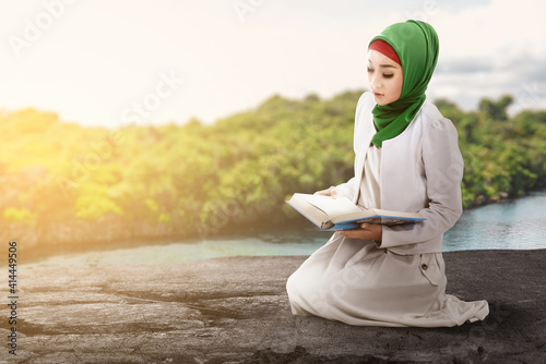 Asian Muslim woman in a veil sitting and reading the Quran
