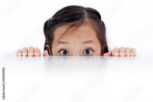 Portrait of an Asian girl peeking through the surface of table isolated on white background.