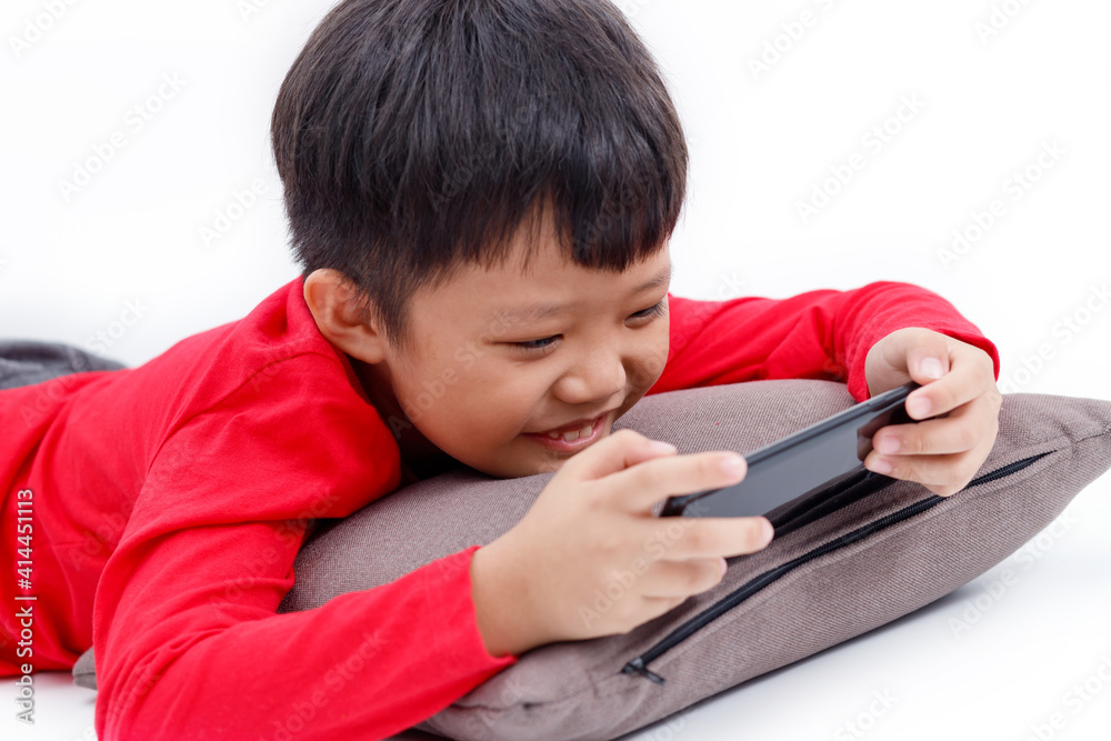Happy little Asian boy lying on a pillow, smiling and using a smartphone at home, isolated on white background. Happy little Asian boy lying on a pillow, smiling and using a smartphone at home, isolated on white background.