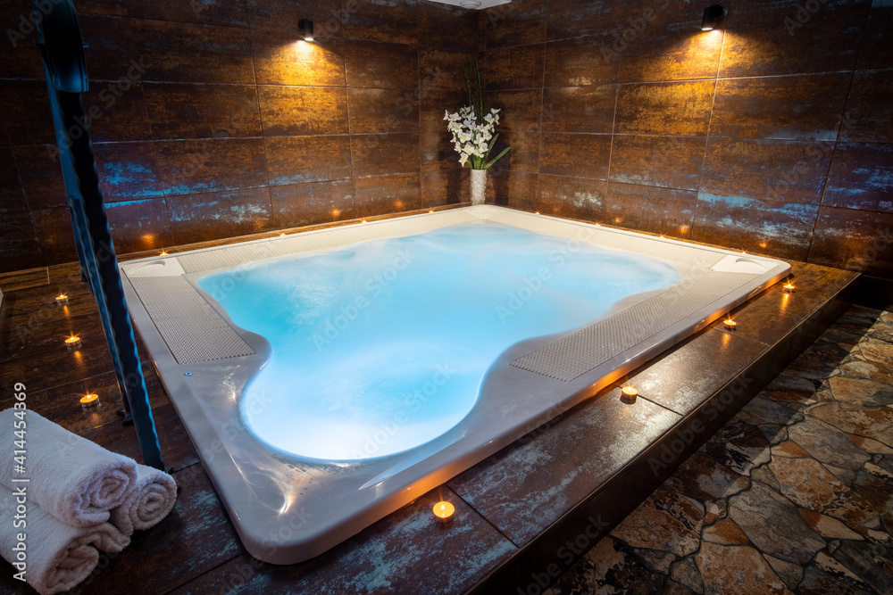 Private whirlpool in a wellness center. Indoor jacuzzi with bubbles. Candles around a whirlpool with blue water.  - obrazy, fototapety, plakaty 