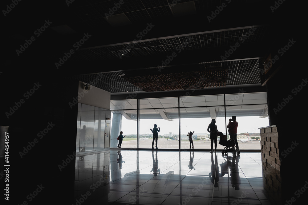 Fototapeta premium Silhouettes of people (family with children) in front of the airport window